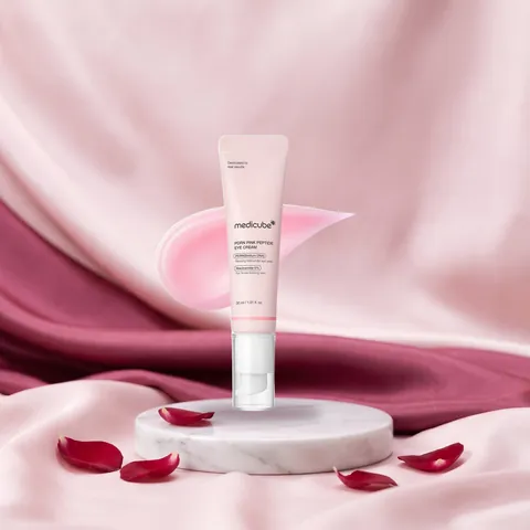 Medicube PDRN Pink Peptide Eye Cream sobre pedestal de mármol con seda rosa